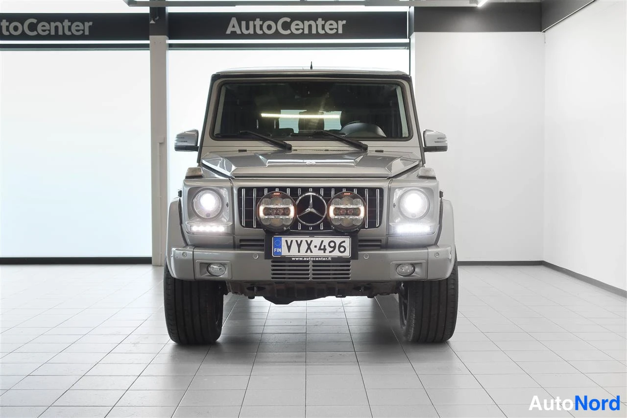 Edestä: Mercedes-Benz G Suoraan edestä kuvattu, lisävalot päällä ja rekisterikilpi näkyvissä.