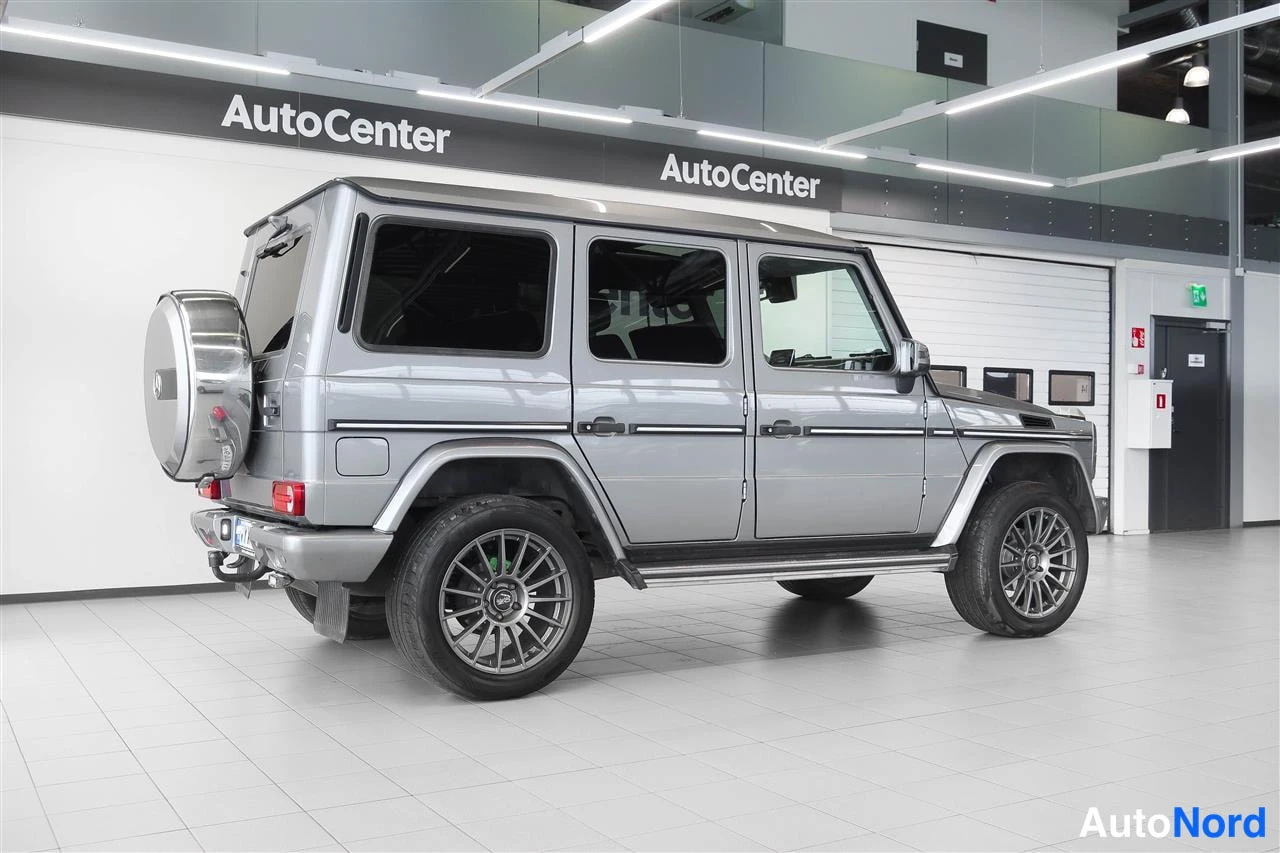 Takaviisto: Hopeanharmaa Mercedes-Benz G takaviistosta kuvattuna autotallin sisällä; takapuskuri, autteessa oleva varapyörä ja kylki näkyvät.