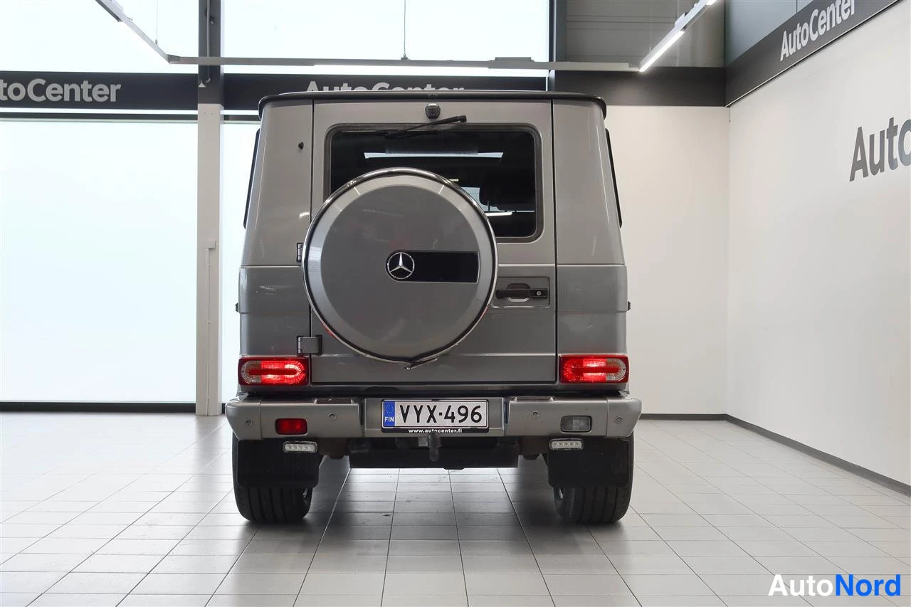 Takaa: Hopeanharmaa Mercedes-Benz G suoraan takaa kuvattuna; varapyörä kannella, takavalot ja rekisterikilpi näkyvät.
