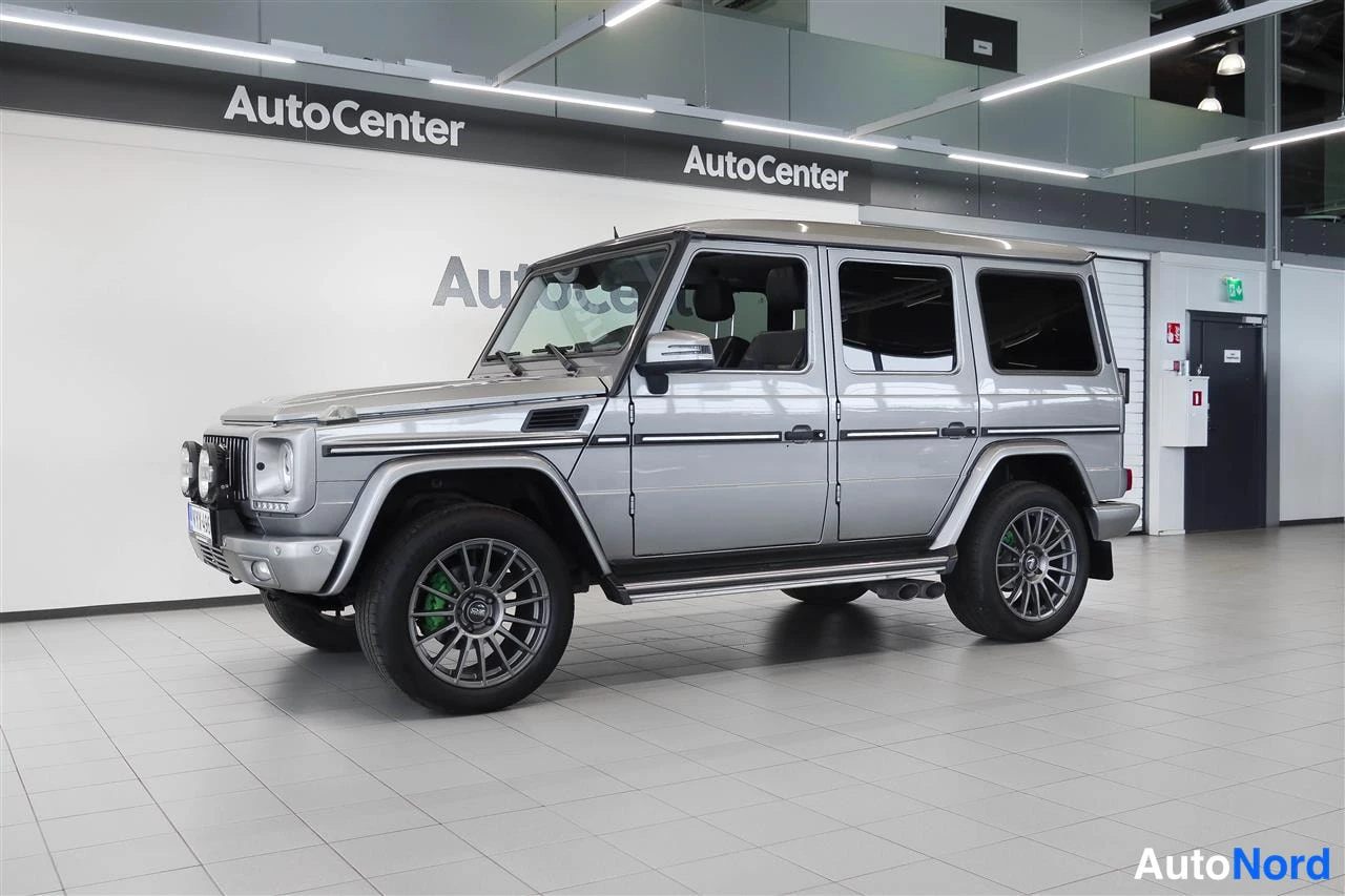 Etuviisto, nokka vasemmalle: Mercedes-Benz G -maasturin hopeanvärinen kori kuvattu kolmanneksesta edestä vasemmalta autonäyttelytilassa.