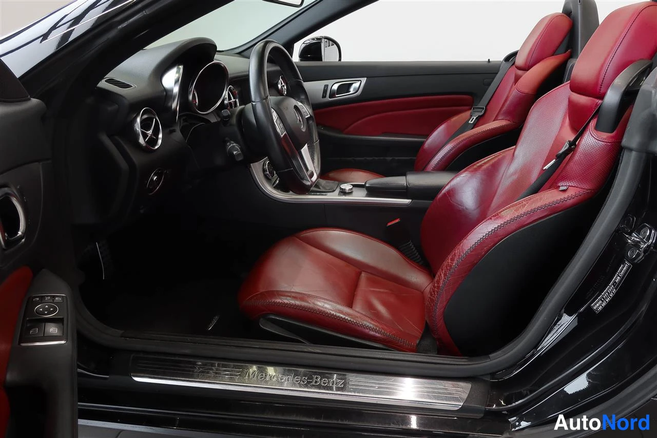 Muu: Avonaisen Mercedes-Benzin sisätila kuljettajan puolen ovesta katsottuna: punaiset nahkaistuimet, ohjauspyörä ja oviaukon kromilista, jossa lukee Mercedes-Benz.