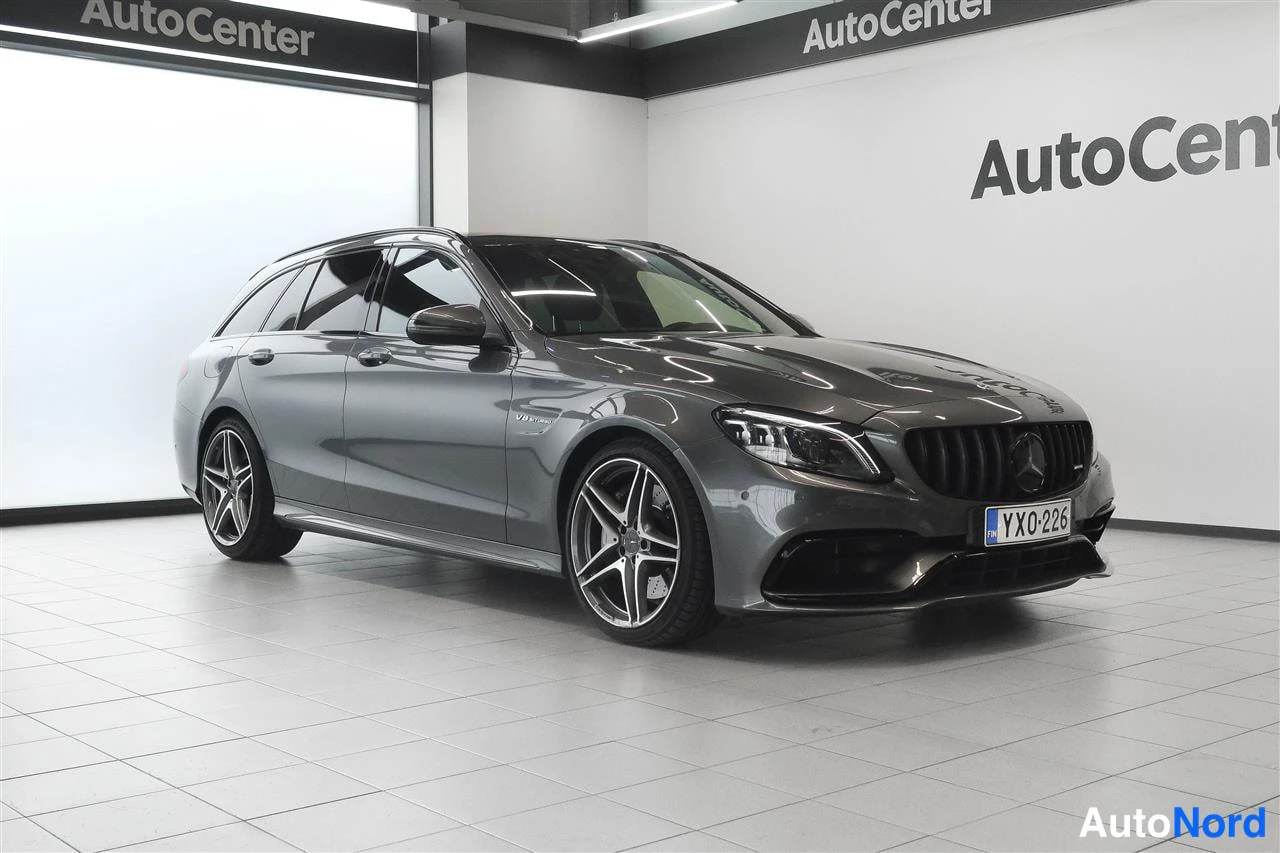 Etuviisto, nokka oikealle: Tummanharmaa Mercedes-Benz farmari kolmeneljännes-etukuvassa oikealta, AutoCenter-merkitty tila, rekisteritunnus.