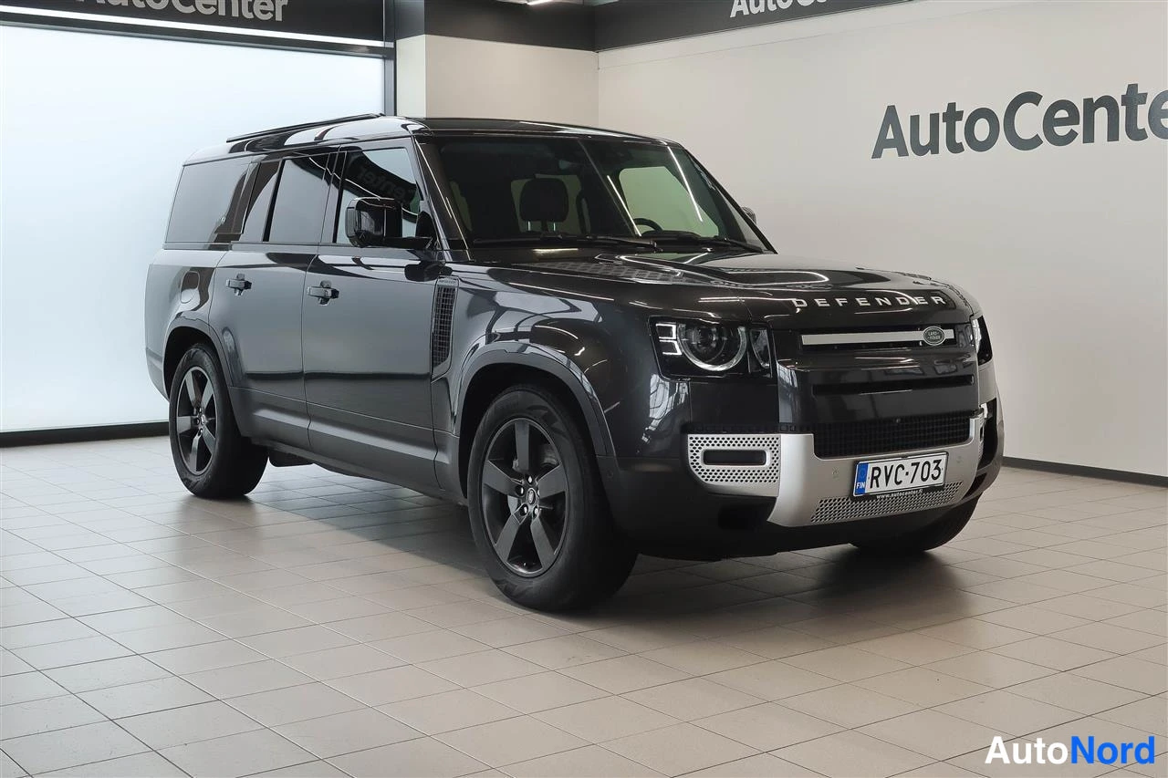 Etuviisto, nokka oikealle: Tummanharmaa Land Rover Defender näkyvissä AutoCenterin showrotilassa, etukulmasta oikeaan eteen.