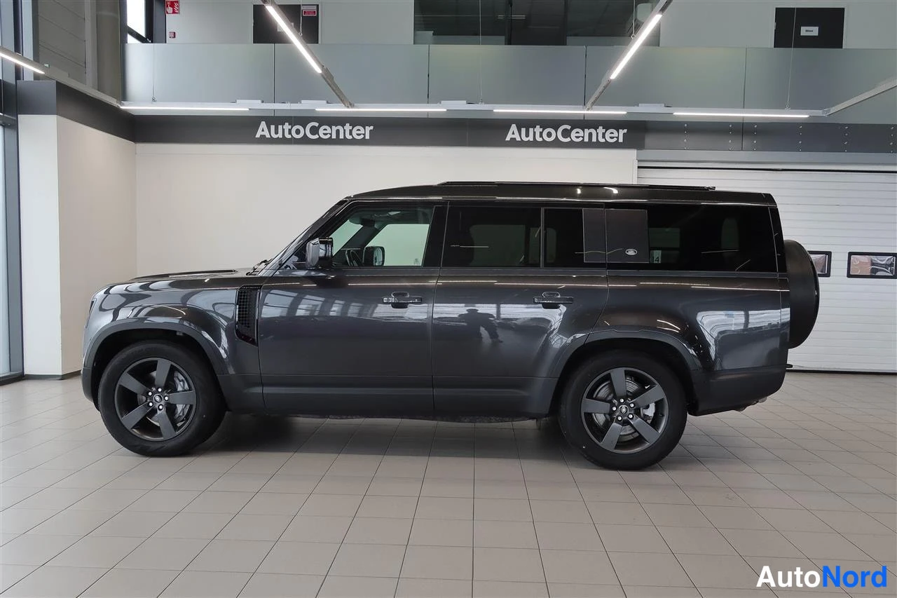 Sivulta: Tummanharmaan Land Rover Defenderin kylkinäkymä showroomissa: viisi ovea ja tummat alumiinivanteet.