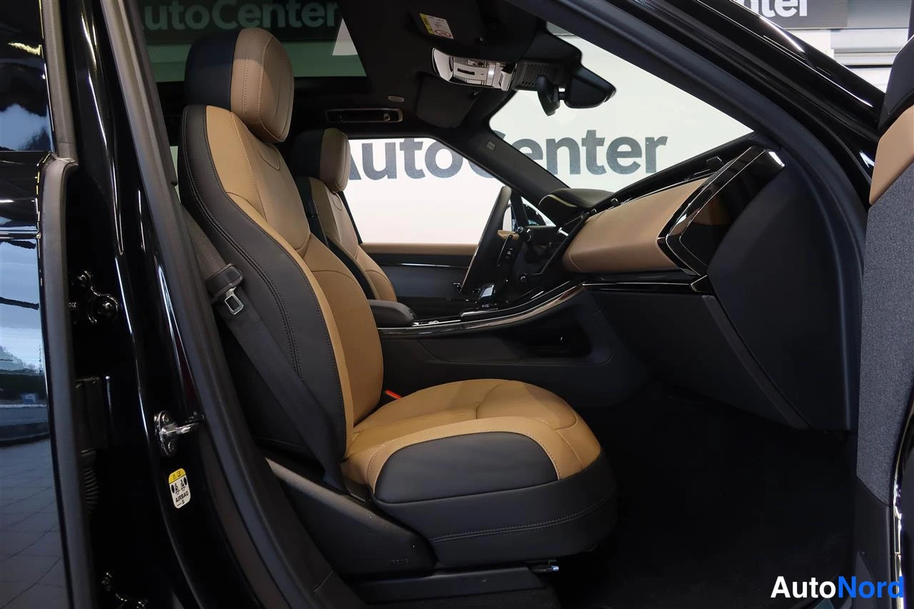 Yksityiskohta: Etumatkustajan istuin tyylikkäässä kaksivärissä, ruskellanruskeassa ja mustassa, keskikäytävän ympäristöineen,AutoCenter-teksti taustalla.