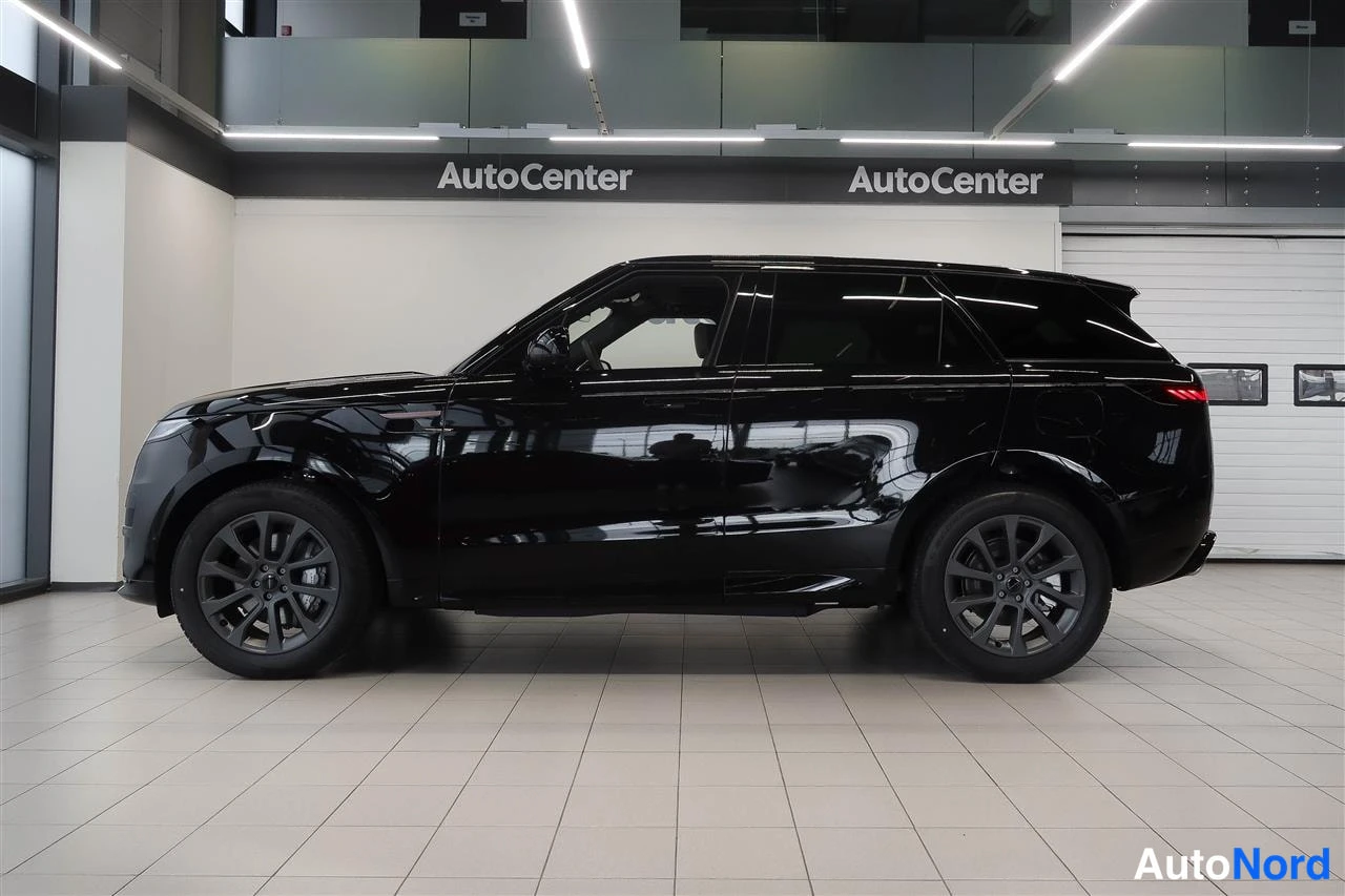 Sivulta: Mustan Range Rover Sportin sivunäkymä autosalon sisällä, auton vasen kylki ja tummat vanteet näkyvät.