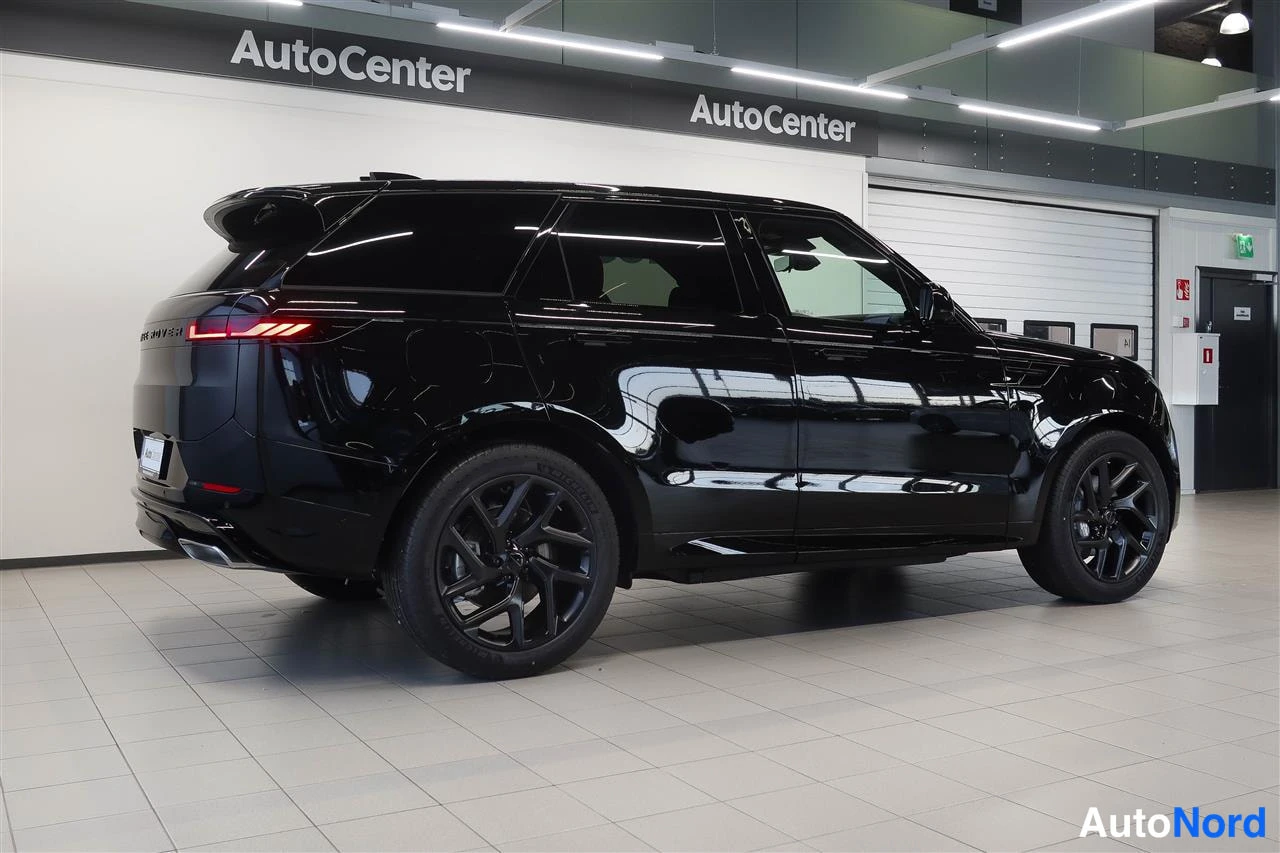 Takaviisto: Musta Land Rover Range Rover Sport takaviisto sisätiloissa, takaosan ja oikean kyljen näkyvissä, tummat vanteet ja AutoCenter-tunnus taustalla.
