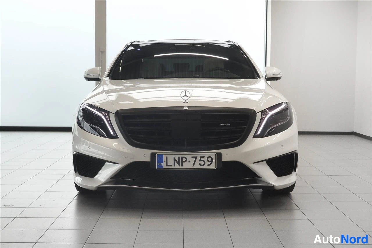 Edestä: Valkoisen Mercedes-Benz S-luokan sedanin etunäkymä sisätiloissa, rekisteritunnus.