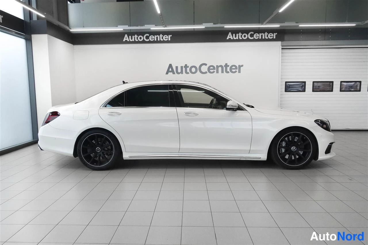 Sivulta: Valkoisen Mercedes-Benz S-luokan sedanin kylkinäkymä sisätiloissa, mustat vanteet.