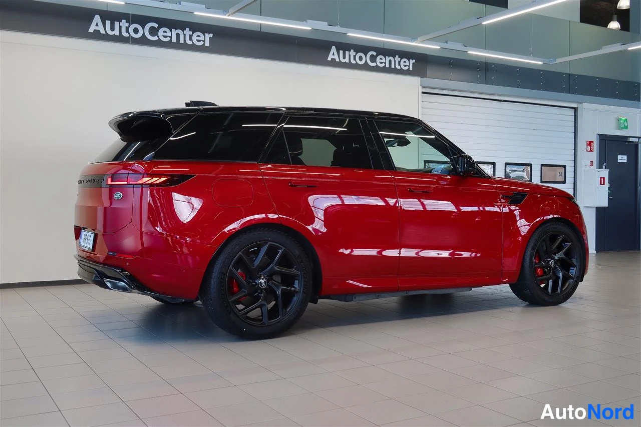 Takaviisto: Punainen Land Rover Range Rover Sport takaa sivusta kuvattuna myymälässä; takavalot, mustat vanteet ja punaiset jarrusatulat näkyvät.