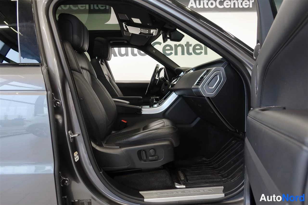 Yksityiskohta: Avaamalla etuovella näkyvä ohjaamomatto: musta nahkainen etuistuin, ovipellin 'LAND ROVER', AutoCenter-logot taustalla.
