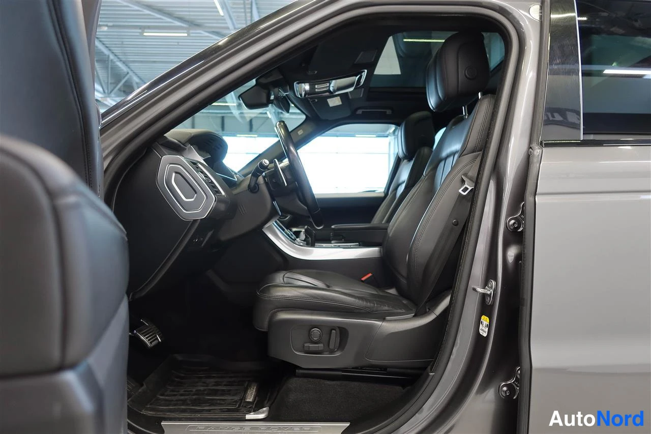 Muu: Range Rover Sportin etusisätilat avoimesta ovesta kuvattuna: mustat nahkaistuimet, ohjauspyörä ja kojelaudan ilmastointisuuttimet näkyvät.