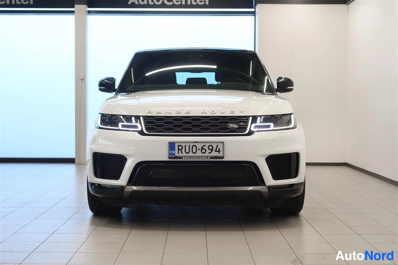 Edestä: Valkoisen Range Rover Sportin etunäkymä, -kilpi, Rangen Rover-teksti konepellillä.