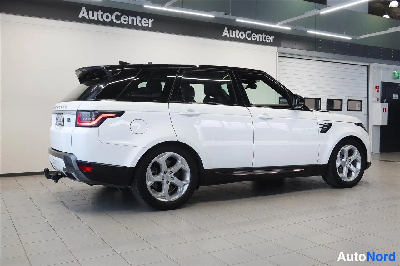 Takaviisto: Valkoinen Range Rover Sport takaa-kulmasta nähtynä autohallissa, musta katto, hopeiset vanteet ja takavetoiskun upotettu kytkin näkyvät.