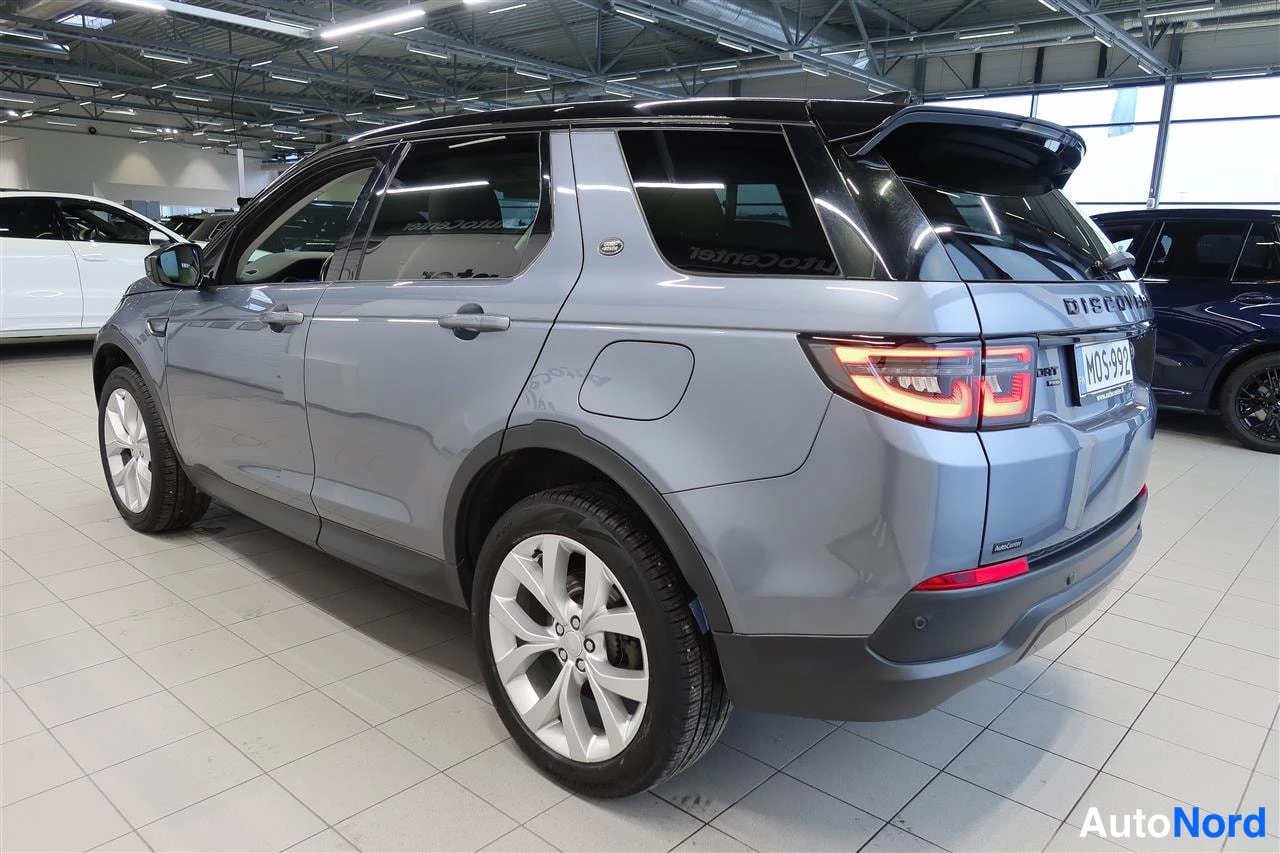 Takaviisto: Land Rover Discovery Sport -maasturin takakulman kuva autosalissa: harmaa kori, musta katto, DISCOVERY-teksti takaluukussa, rekisterikilpi.