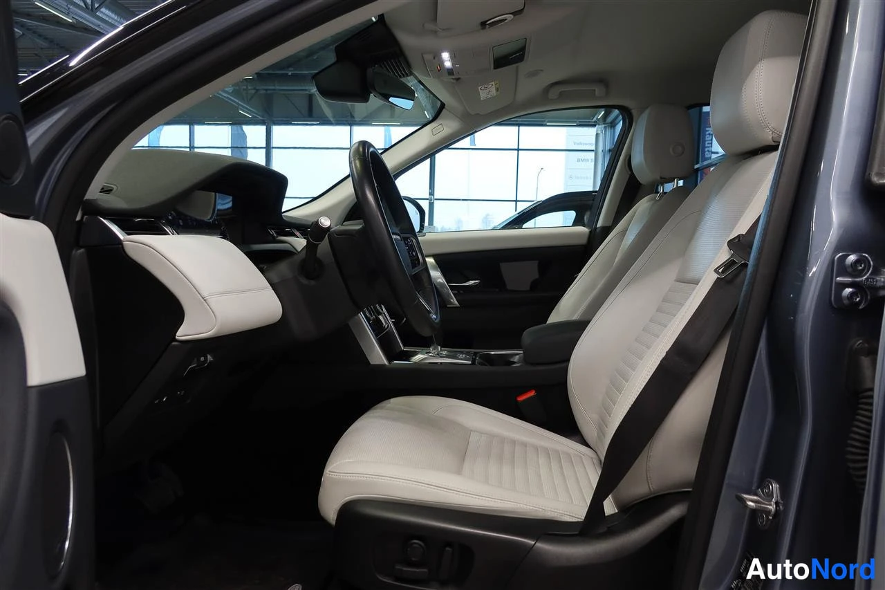 Muu: Land Rover Discovery Sportin etuistuin ja kojelauta sivulta: vaalea nahkaverhoilu, ohjauspyörä ja keskinäyttö näkyvät.