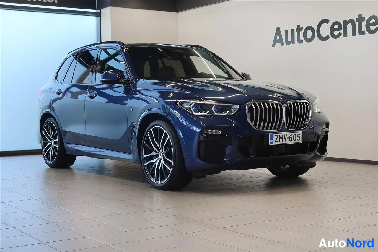Etuviisto, nokka oikealle: Sininen BMW X5 esillä AutoCenter-tilassa, etukulmanäkuva oikeaan كäännytettynä, rekisteritunnus.