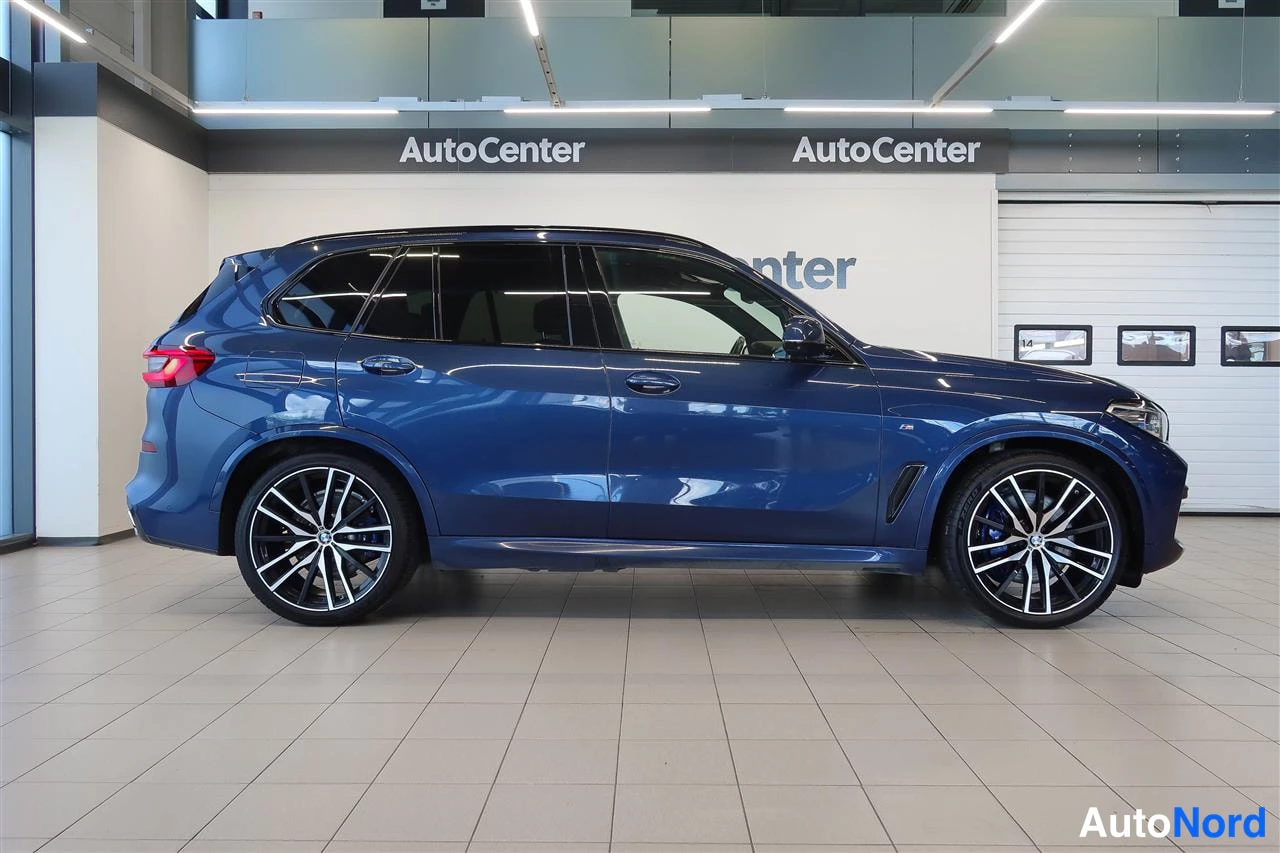 Takaviisto: Sivukulmakuva tummansinisestä BMW X5 -maasturista sisätiloissa, takavalo ja kylki näkyvissä.