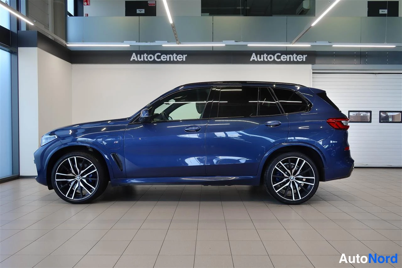 Sivulta: BMW X5:n vasen sivu; sininen maali, mustat ikkunat ja monihapsiset kevytmetallivanteet näkyvät sisätiloissa.