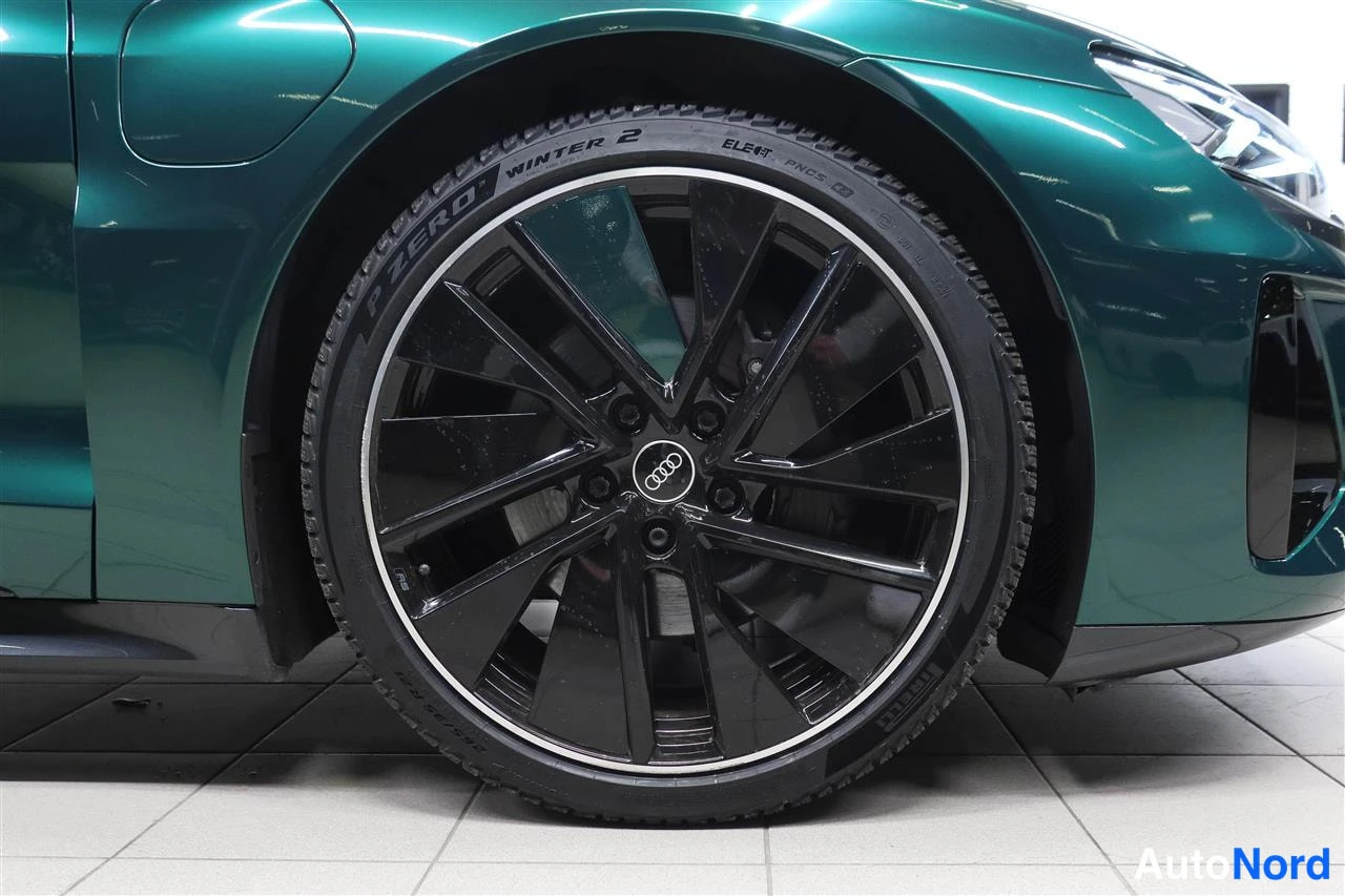 Etuviisto, nokka oikealle: Lähikuva tummanvihreän auton etupyörästä: musta Audi-vanteen kevytmetallivanne ja Pirelli Winter 2 -talvirengas.