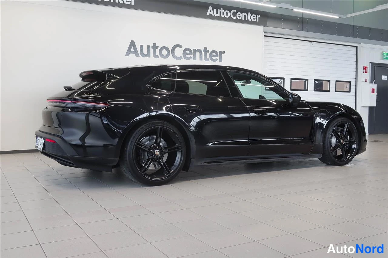 Takaviisto: Mustan Porsche Taycan Sport Turismo -farmarin takakolmasosanäkuva sisätilassa, punainen takavalonpoikki ja mustat kevytmetallivanteet näkyvissä.