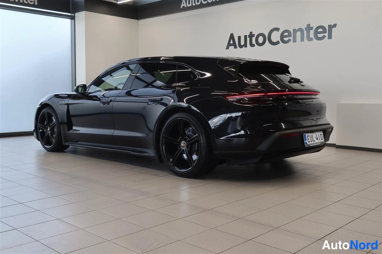 Takaviisto: Mustan Porsche Taycan -automobiilin takakolmasosanäkuva sisätilassa, punainen takavalonpoikki, mustat kevytmetallivanteet ja rekisterikilpi näkyvissä.