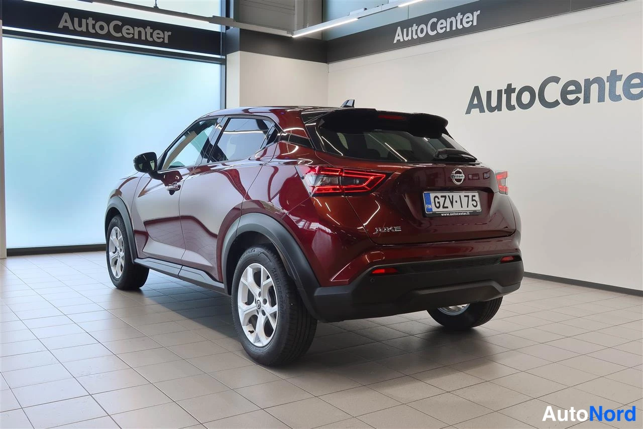Takaviisto: Tummanpunaisen Nissan Juken takakulma autosalissa, rekisterikilpi.