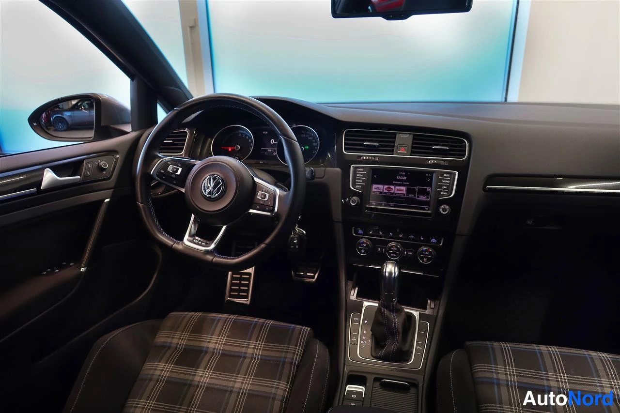 Muu: Näkymä Volkswagenin ohjaamoon: VW-merkkinen ohjauspyörä, mittaristo, keskikonsolin radio ja vaihtaja sekä ruutuilliset etuistuimet.