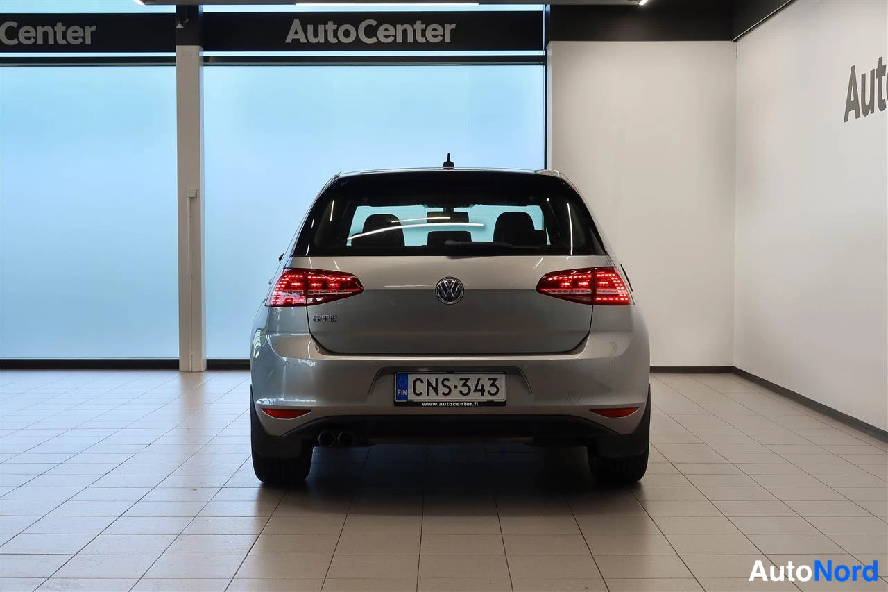 Takaa: Auton takaosan suorakuva sisätiloissa; rekisterikilpi, takavaloja ja VW-merkki näkyvissä.