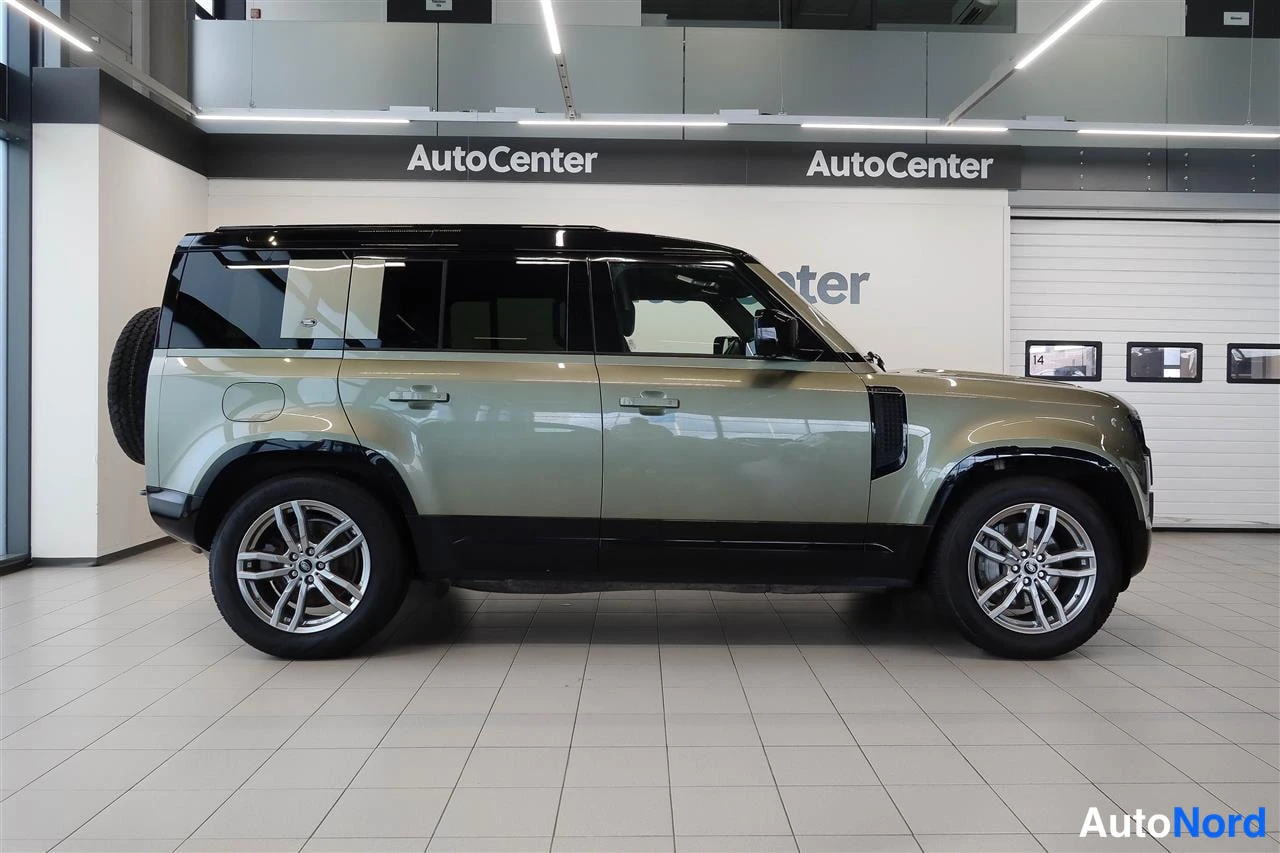 Sivulta: Land Rover Defender oliivinvihreä sivulta vasemmalta, takana varapyörä, AutoCenter-tilassa