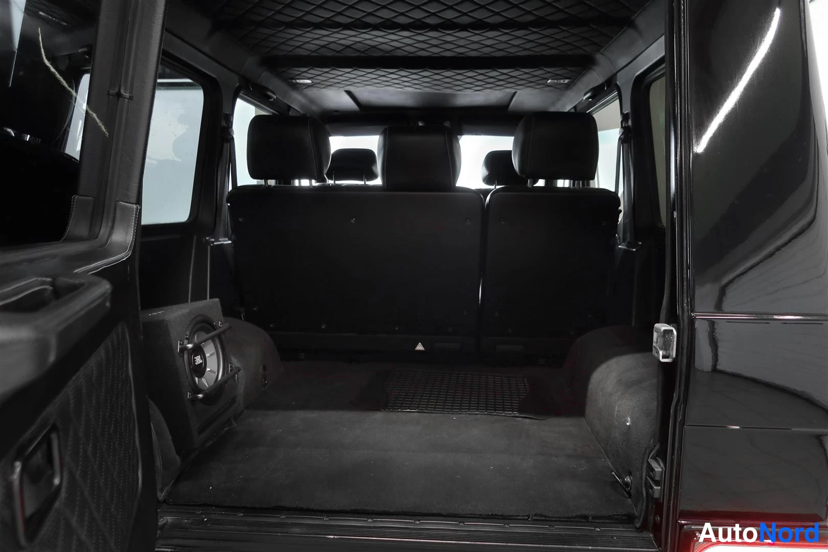Yksityiskohta: Mercedes-Benz G:n tavaratila ja takapenkin selkänojat avatusta takaluukusta kuvattuna; subwoofer-kotelo tavaratilan vasemmassa reunassa.