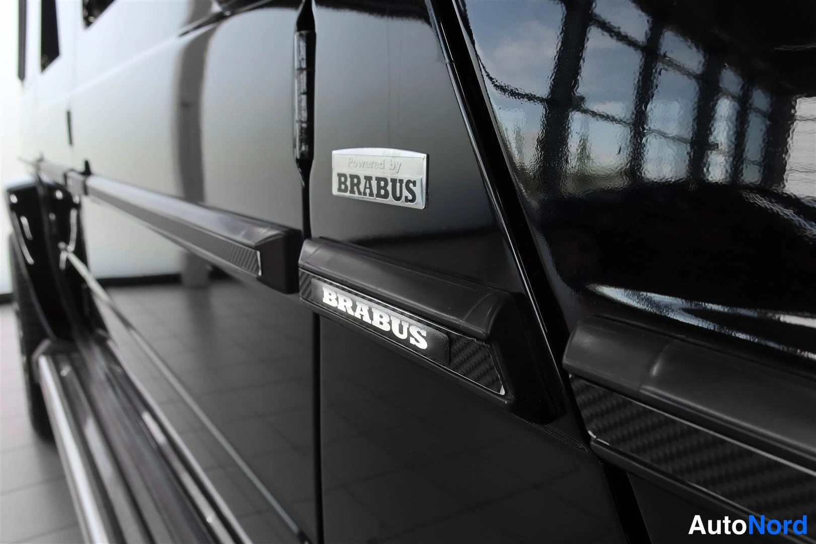 Yksityiskohta: Mustan Mercedes-Benz G:n sivupaneelin lähikuva, jossa näkyvät BRABUS-tarrat ja ovilista.