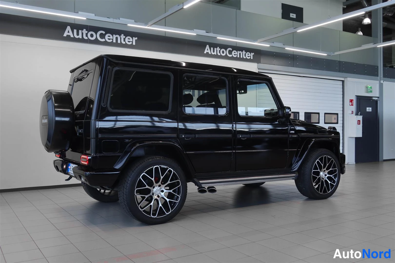 Takaviisto: Musta Mercedes-Benz G -maasturi takaa sivulta kuvattuna, varapyörä takaluukussa ja kaksoispakoputket.