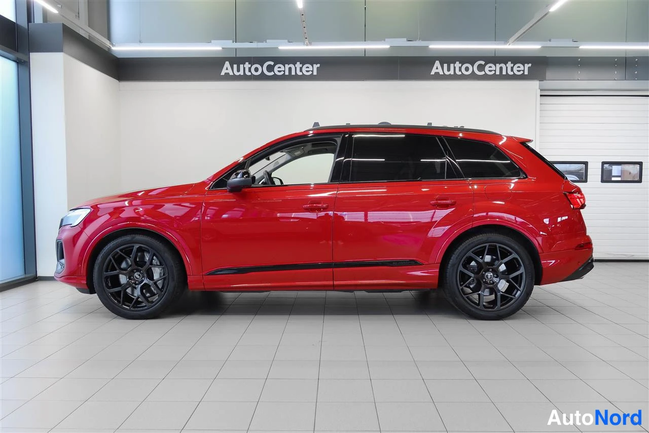 Sivulta: Punaisen Audi Q7:n sivuprofiilinäkymä sisätilassa, mustat kevytmetallivanteet näkyvät.
