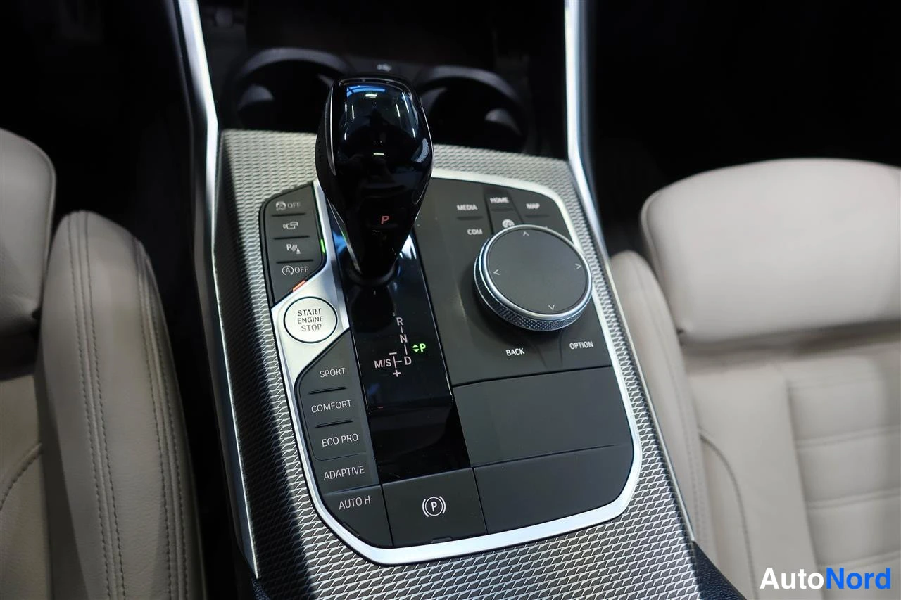 Sivulta: Lähikuva auton keskikäytävästä: automaattivaihteen vaihdekeppi, START ENGINE STOP -painike, iDrive-kiertokytkin sekä ajotilapainikkeet SPORT, COMFORT, ECO PRO j