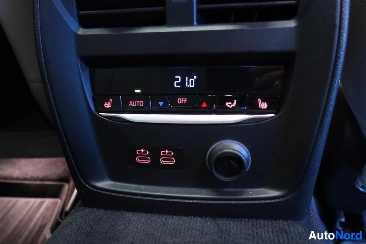 Muu: Auton takapenkin etupaneelin ilmastointipaneeli: näytössä 21°, napit AUTO ja OFF, penkkilämmitys- ja tuuletussymbolit sekä 12 V pistorasia.