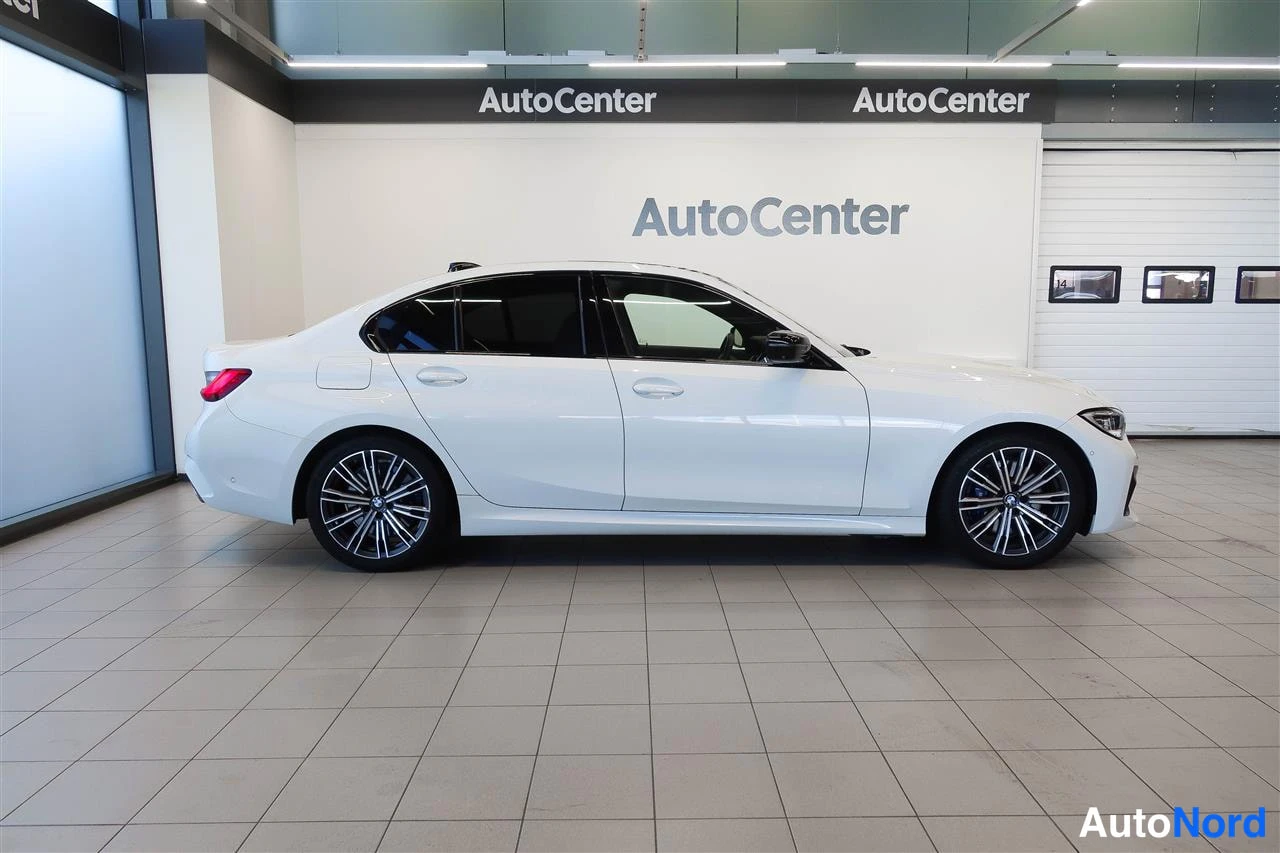 Takaviisto: Valkoinen BMW 330 -sedan sivusta takakolmannesnäkymässä AutoCenter-hallissa.
