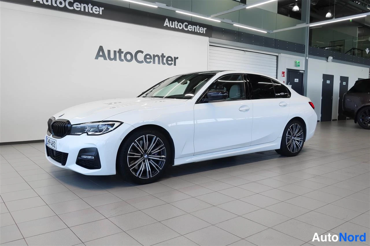 Etuviisto, nokka vasemmalle: Valkoinen BMW 330 -sedan etukolmannesnäkymä, keulakko vasemmalla, AutoCenter-hallissa.