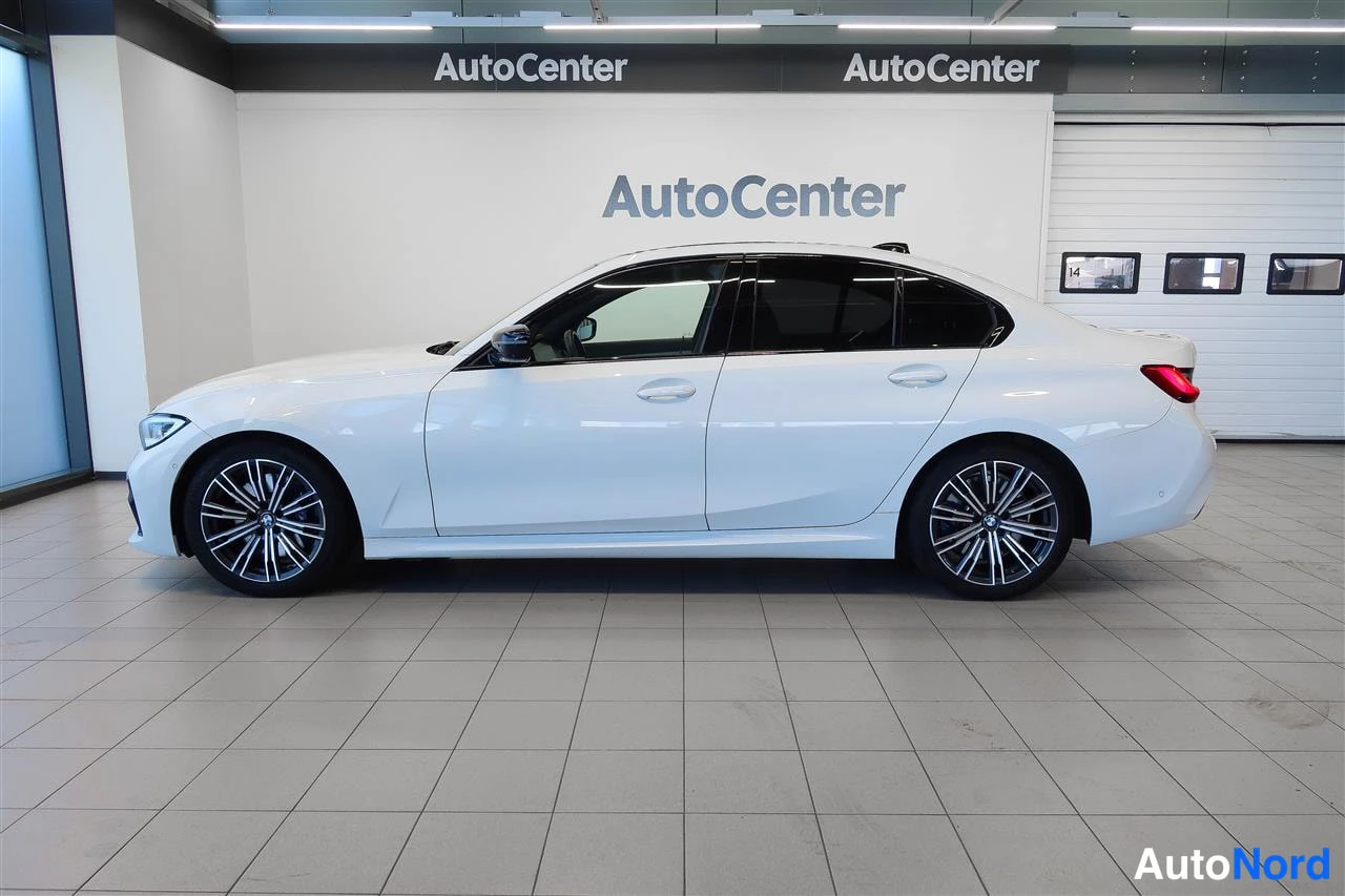 Etuviisto, nokka vasemmalle: Valkoinen BMW 330 -sedan kyljenäkymä keula vasemmalla, AutoCenter-hallissa.