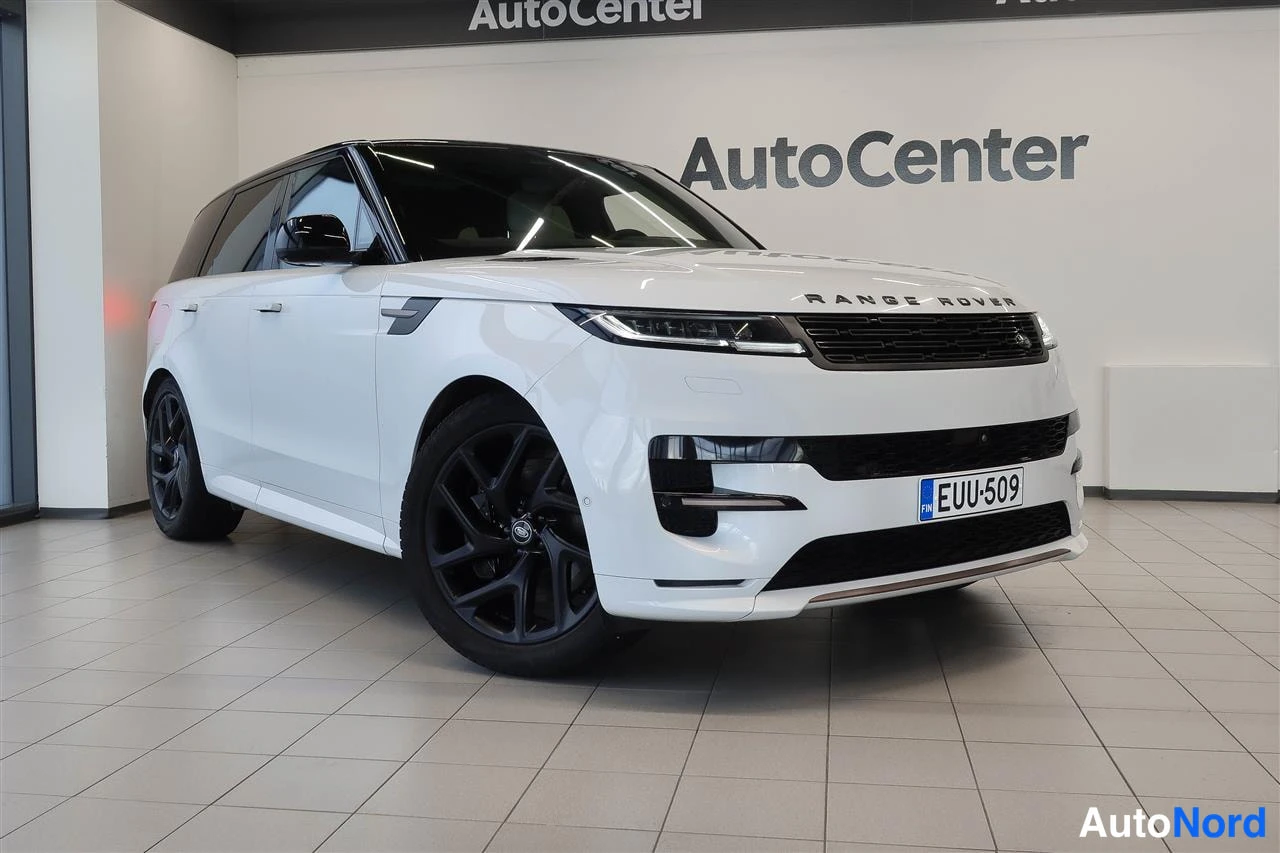 Etuviisto, nokka oikealle: Valkoinen Land Rover Range Rover Sport -maastauto sisätiloissa, edestä kolmannelta sivulta kuvattu; mustat kevytmetallivanteet ja rekisterikilpi.
