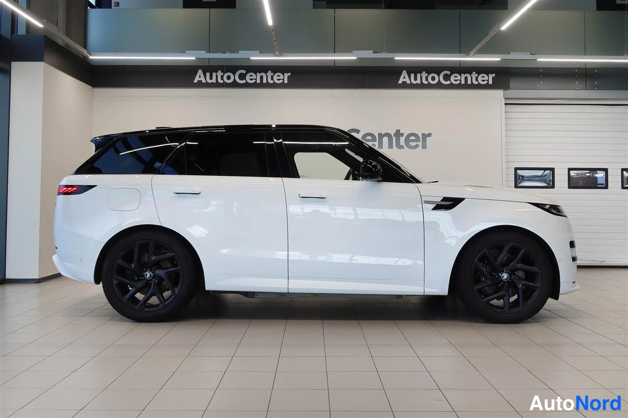 Sivulta: Valkoisen Land Rover Range Rover Sportin kylkinäkymä oikealta sivulta sisätiloissa; musta lasikatto ja mustat kevytmetallivanteet.
