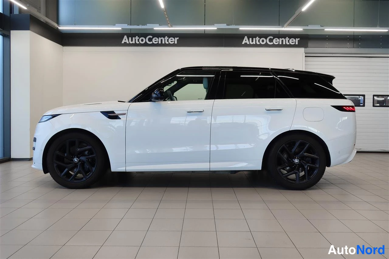 Etuviisto, nokka vasemmalle: Valkoinen Land Rover Range Rover Sport sivulta vasemmalta nähtynä mustalla katolla ja mustilla vanteilla AutoCenter-hallissa.