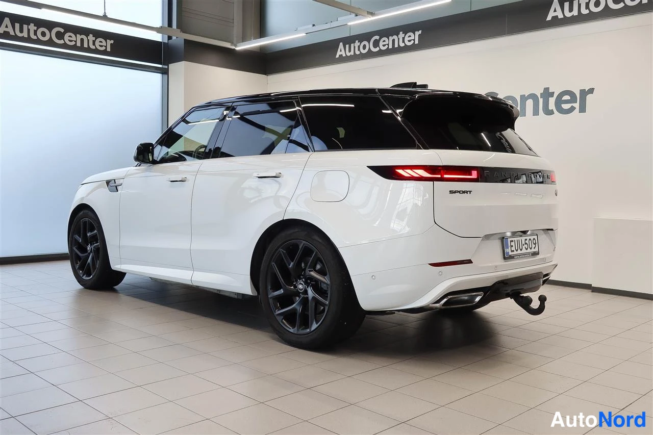 Takaviisto: Valkoinen Land Rover Range Rover Sport takaviistosta oikealta nähtynä mustalla katolla, rekisterikilvellä ja kiinnityshakalla AutoCenter-hallissa.