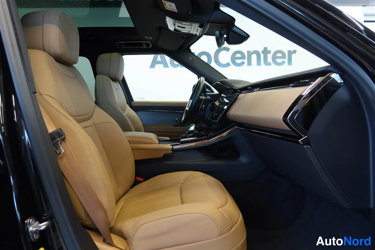 Yksityiskohta: Auton etusohva sivulta: beige-tan keinonahkaiset etuistuimet, tumma kojelauta ja keskitaso, taustalla AutoCenter-logon ikkuna.