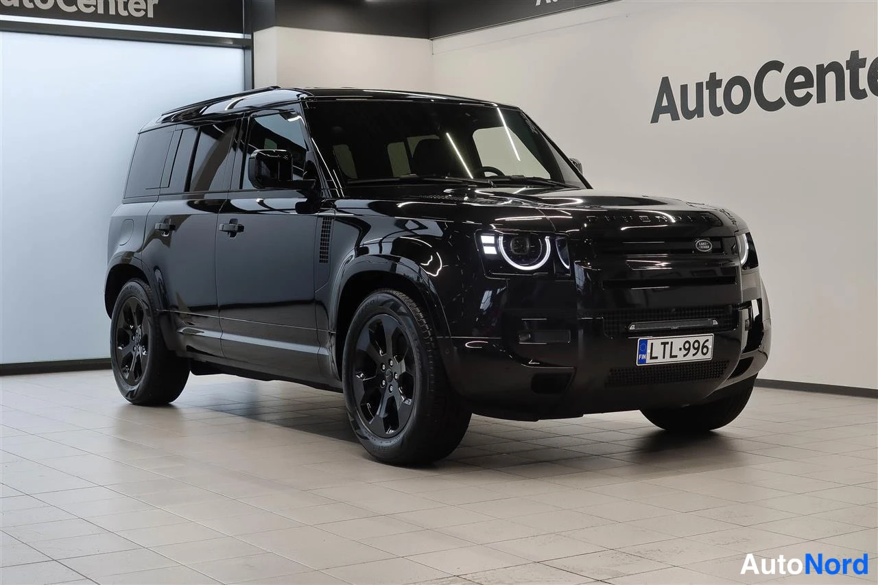 Etuviisto, nokka oikealle: Musta Land Rover Defender etukulmasta oikealta kuvattuna, LED-ajovalot päällä.