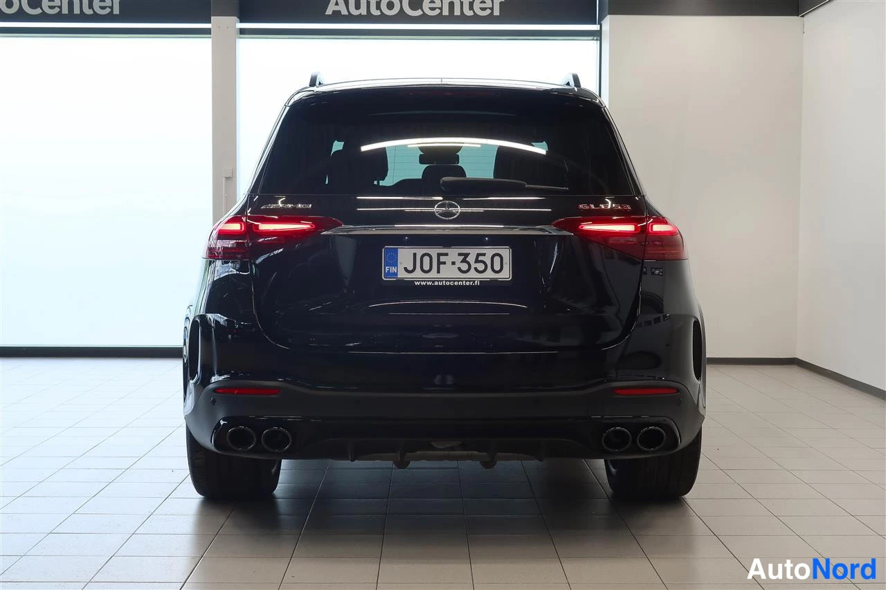 Takaa: Musta Mercedes-Benz GLE 53 AMG -maastonauton takanäkymä sisätiloissa, rekisterikilpi J0F-350, neljä pakoputkea ja kannessa kattotelineet.