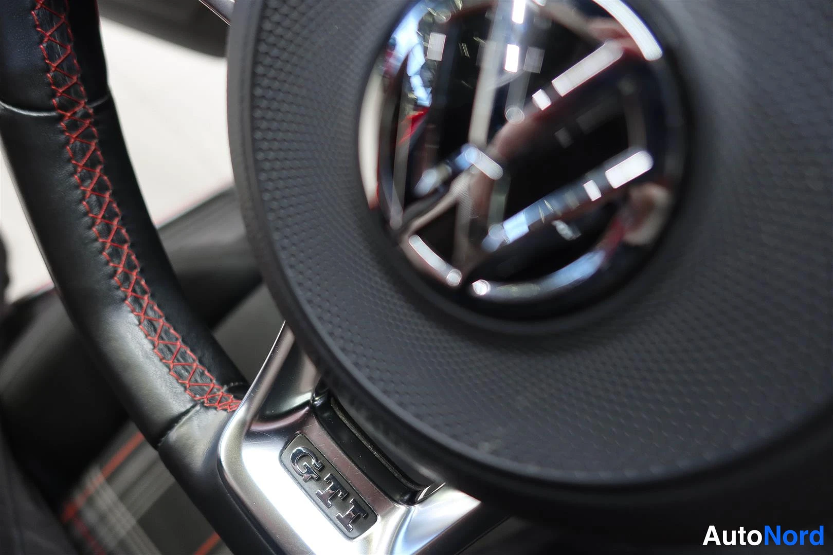 Muu: Ohjauspyörän close-up: Volkswagen-merkki keskellä ja GTI-merkki alhaalla, punakirjontainen koriste ompelu ohjauspyörän renkaassa.