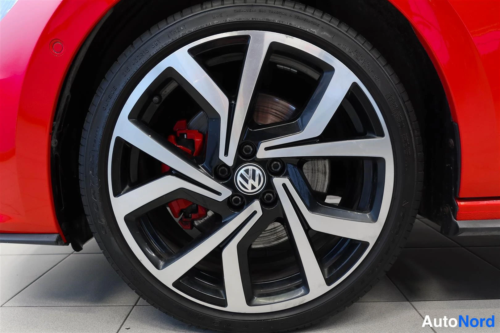 Sivulta: Punaisen auton aluvannas lähikuvassa, VW-merkki napassa ja punainen jarrusatula näkyvissä.