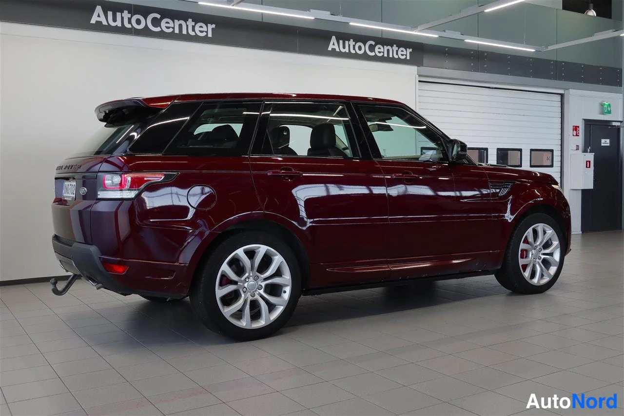 Takaviisto: Tummankeltaista? ei – tummanpunaisen Range Rover Sport -maasturin takakolmannes sisätiloissa, taustavalo ja takarenkaat näkyvät, lossivaijeri takapuskurissa.