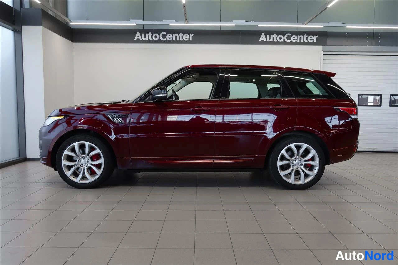 Sivulta: Tummanpunaisen Range Rover Sportin sivuprofiili sisätiloissa, kummankin akselin hopeavanteet näkyvät.
